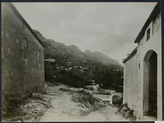 Rocky village street in Lapithos with whitewashed buildings, trees and mountains rising behind