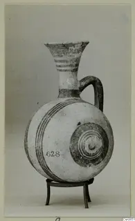 Painted pottery juglet with a flaring neck and single loop handle, standing on a metal tripod stand.
