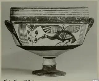Painted pottery vessel on a high foot, with a dark bird and plant motif between bands, photographed against a grey backdrop