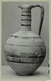 Bichrome IV jug with dark painted bands, a strap handle and a pinched spout, against a grey backdrop