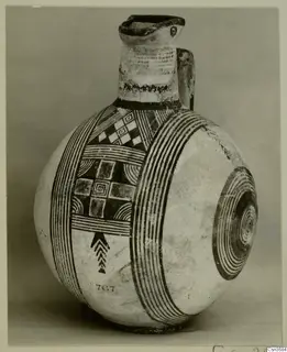Painted pottery jug with a tall neck, a side loop handle and bands of dark concentric and geometric patterns on a pale body.