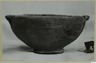 Grey polished ware bowl with a flaring rim, a small lug and a low ring foot, photographed from the side