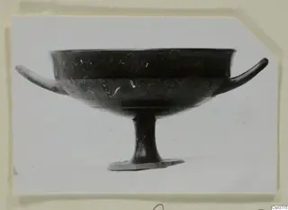 Footed bowl with two thin horizontal handles and a dark surface, photographed in side view against a white background.