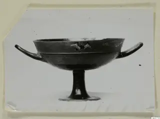 Stemmed bowl with two horizontal handles and a small painted bird-like figure with spread wings on its side.