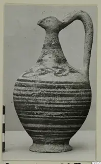 Painted pottery jug with a bird-head spout and strap handle, beside a scale bar