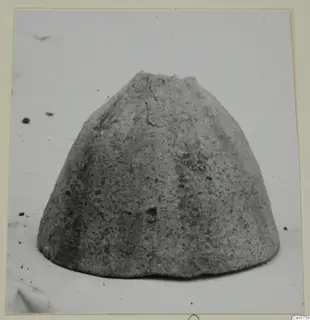 Grey, rough-surfaced dome-shaped object with a broken flat top, photographed alone on a pale background