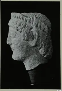 Carved limestone head from Mersinaki, shown in profile facing left, with curled hair and the ear visible.