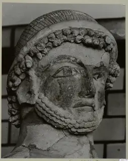 Close-up of a sculpted head with a ridged cap, rows of curled locks and a curled beard, Terracotta Cypro-Greek II