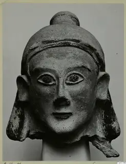 Terracotta head with a tall rounded cap, large projecting ears and flaring side locks, shown on a plain support