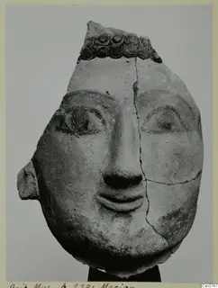 Terracotta head with painted eyes and brows, from Mersinaki, with a band of circular ornament across the top.