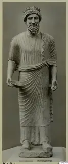 Limestone statue of a bearded standing man wearing a leaf wreath and holding a shallow bowl, from Arsos