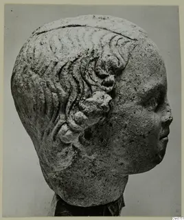 Carved stone head from Mersinaki, shown in profile facing right, with wavy hair and rounded curls above the ear.
