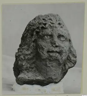 Stone head from Soli with wavy hair and worn facial features, on a white base.