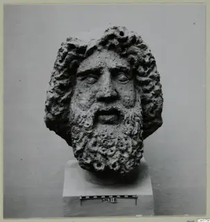 Bearded stone head from Soli on a square plinth, with a scale bar at its base
