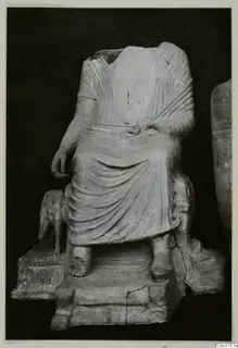 Headless seated figure in a draped garment on a stepped base, with a small animal figure at its left side.
