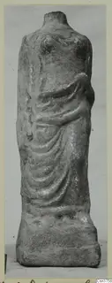 Headless draped statue fragment of grey stone standing on a rectangular base