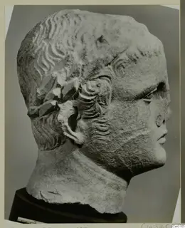 Carved stone head in profile, with wavy hair and a band across it above the ear.