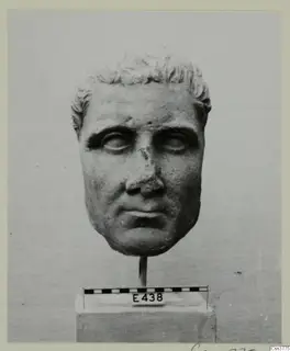 Roman sculpture: stone head of a man with short curled hair, mounted on a rod above a base with a scale bar.