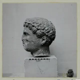 Roman sculpture: carved stone head with rows of curled hair, set on a block beside a scale bar