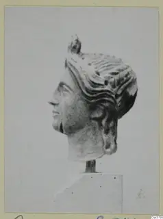 Stone head in profile with wavy hair drawn back to a knot at the crown, mounted on a block base