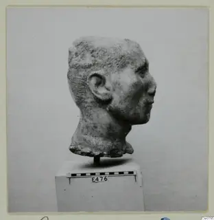 Stone head of a figure in profile, set on a pedestal beside a scale bar.