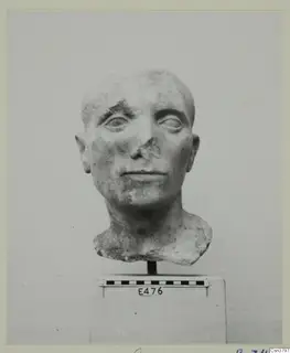Roman stone sculpture of a man's head with a damaged nose, on a block with a scale bar