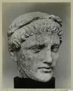 Stone head of a young man with short curled hair bound by a band, resting on a dark cylindrical base