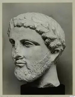 Carved stone head of a bearded man with curled hair, on a dark cylindrical base; the nose is chipped.
