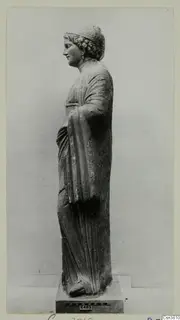 Draped stone statue of a standing figure, seen in profile on a square base.