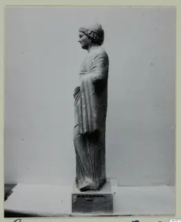 Standing stone statue of a female figure, seen in profile facing left, on a square base