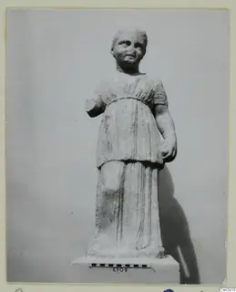Stone statue of a standing figure in a short-sleeved belted tunic, on a plinth with a scale bar