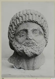 Carved stone head of a bearded man with rows of curls, shown in an old photograph mounted on a card