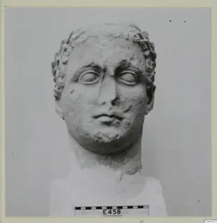 Stone head with curled hair and a scale bar, shown against a plain grey backdrop.