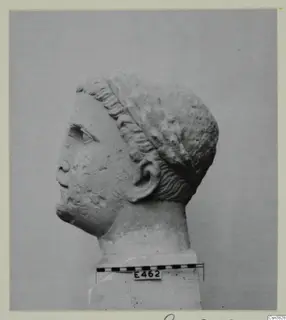 Stone head in profile facing left, with wavy hair swept back from the brow, on a block base beside a scale bar.