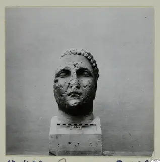 Stone head of a figure on a square plinth, with a scale bar and number label E462 fixed to the base
