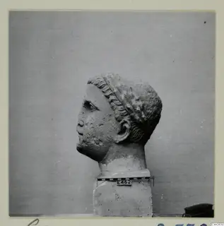 Stone head sculpture in profile, facing left, on a square base beside a scale bar.