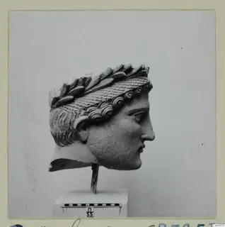 Stone head in profile facing right, with a wreath of leaves and curled hair, on a stand