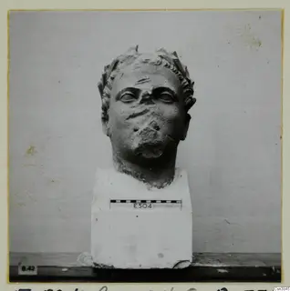 Carved stone head on a square block base, with a scale bar and number label E504 on the base