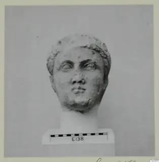 Carved stone head with curled hair, set on a plinth beside a scale bar.