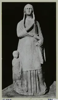 Standing draped female statue with a veil, with a small child figure at her side, photographed against a black background