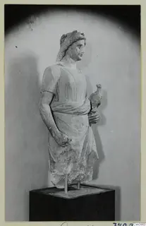 Stone statue of a standing figure with a wreath in its hair, holding a small bird