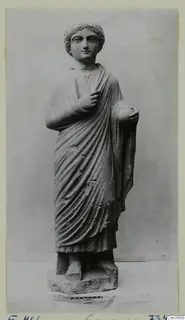 Standing draped stone statue of a young figure with short curled hair, mounted on a rectangular base.