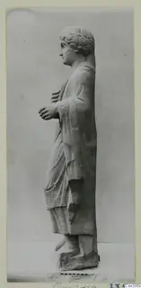 Stone statue of a standing figure in a draped cloak, shown in profile facing left