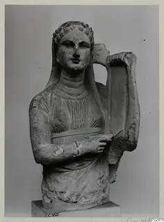 Stone statue of a female figure with curled hair and a veil, holding a lyre-shaped instrument beside her shoulder