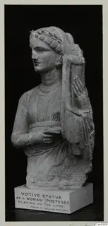 Stone statue of a woman with a lyre, photographed against a black background on a plinth with a printed label.