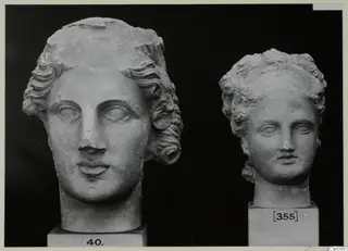 Two sculpted heads with curled, wavy hair, each on a square plinth, shown against a black background.