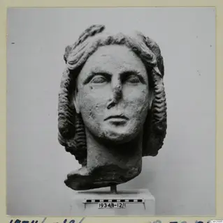 Carved stone head of a woman with wavy hair, set on a short stand in front of a scale bar