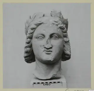 Sculpted stone head with wavy hair and a leaf wreath, on a square base with a scale bar