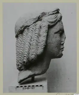Carved stone head in profile facing right, with hair in rows of wavy curls, standing on a block base