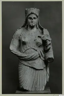 Stone statue of a female figure with a tall headdress and draped garment, holding a cylindrical object against her side